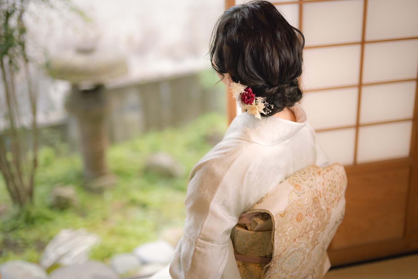 Người phụ nữ mặc kimono ngồi ở hiên nhà Nhật nhìn ra vườn, chụp từ phía sau