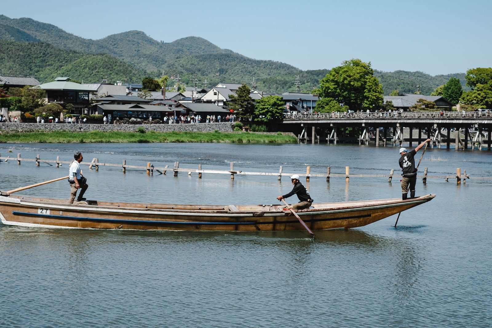 Thuyền gỗ chở khách trôi trên sông Katsura trước cầu Togetsukyo và dãy núi Arashiyama, Kyoto